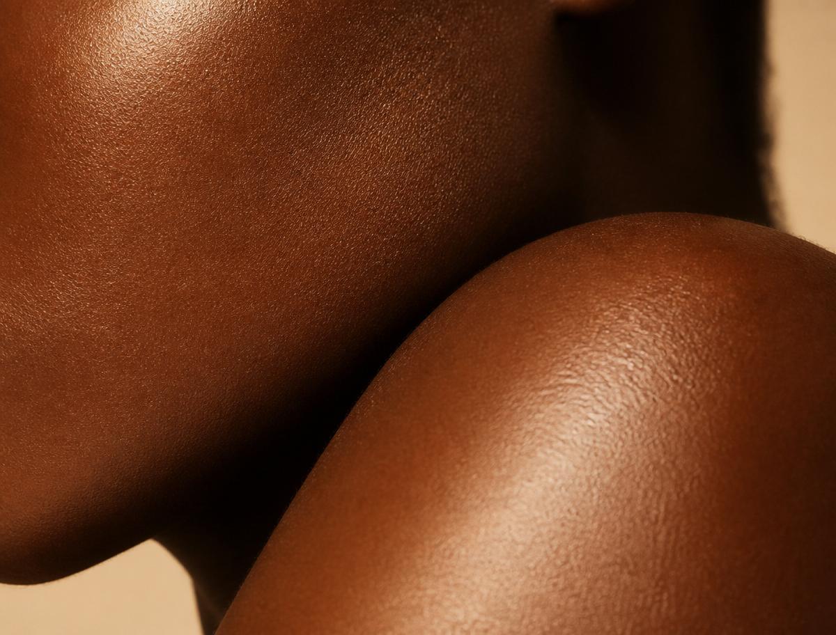 Close-up of healthy, glowing deep brown skin in warm ivory light